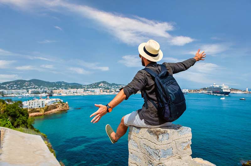 A guy sitting on the edge of stone structure looking at the sea in front of him
